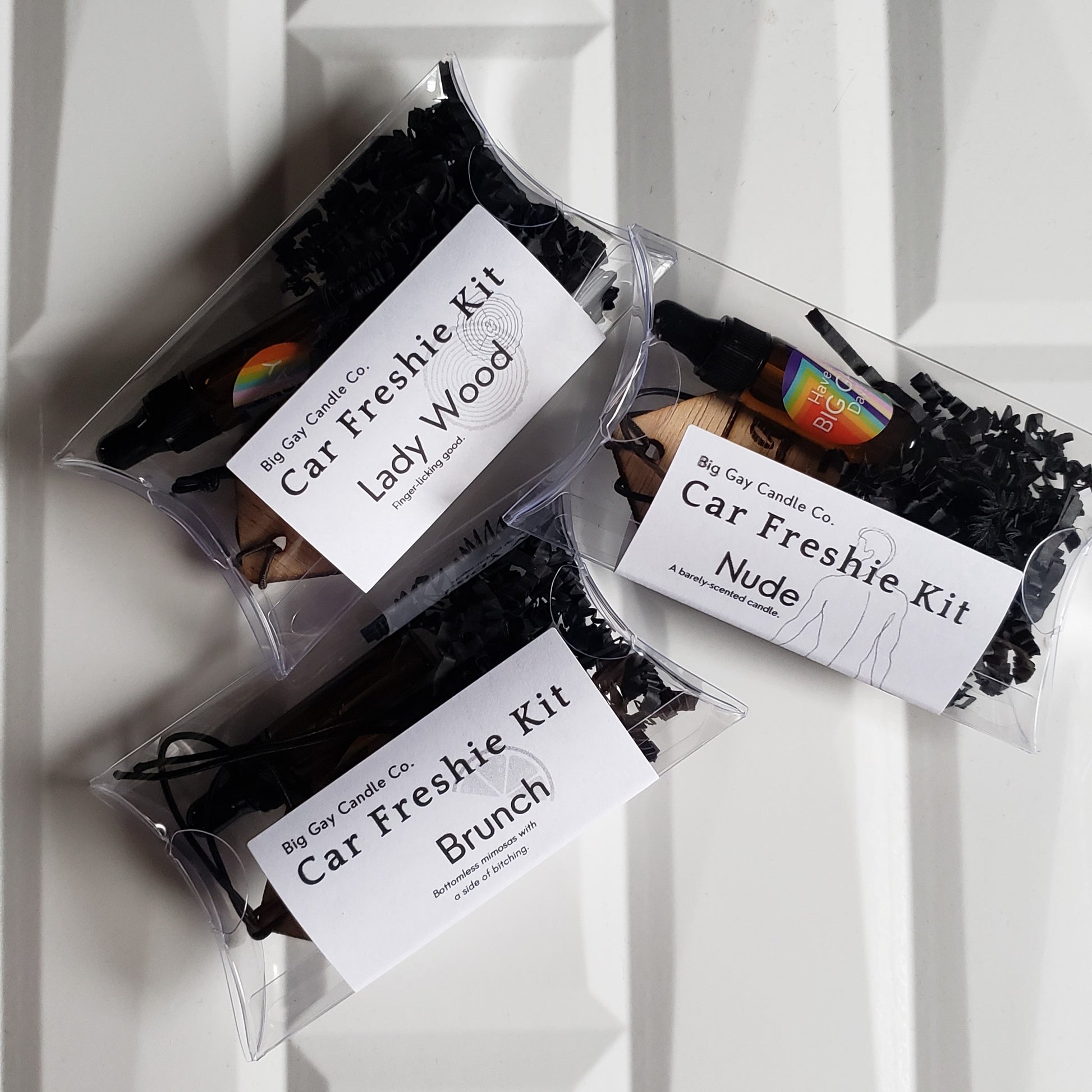 Overhead picture of a white tile background with plastic pillow boxes with a black and white label with the names Lady Wood, Nude, and Brunch on top.